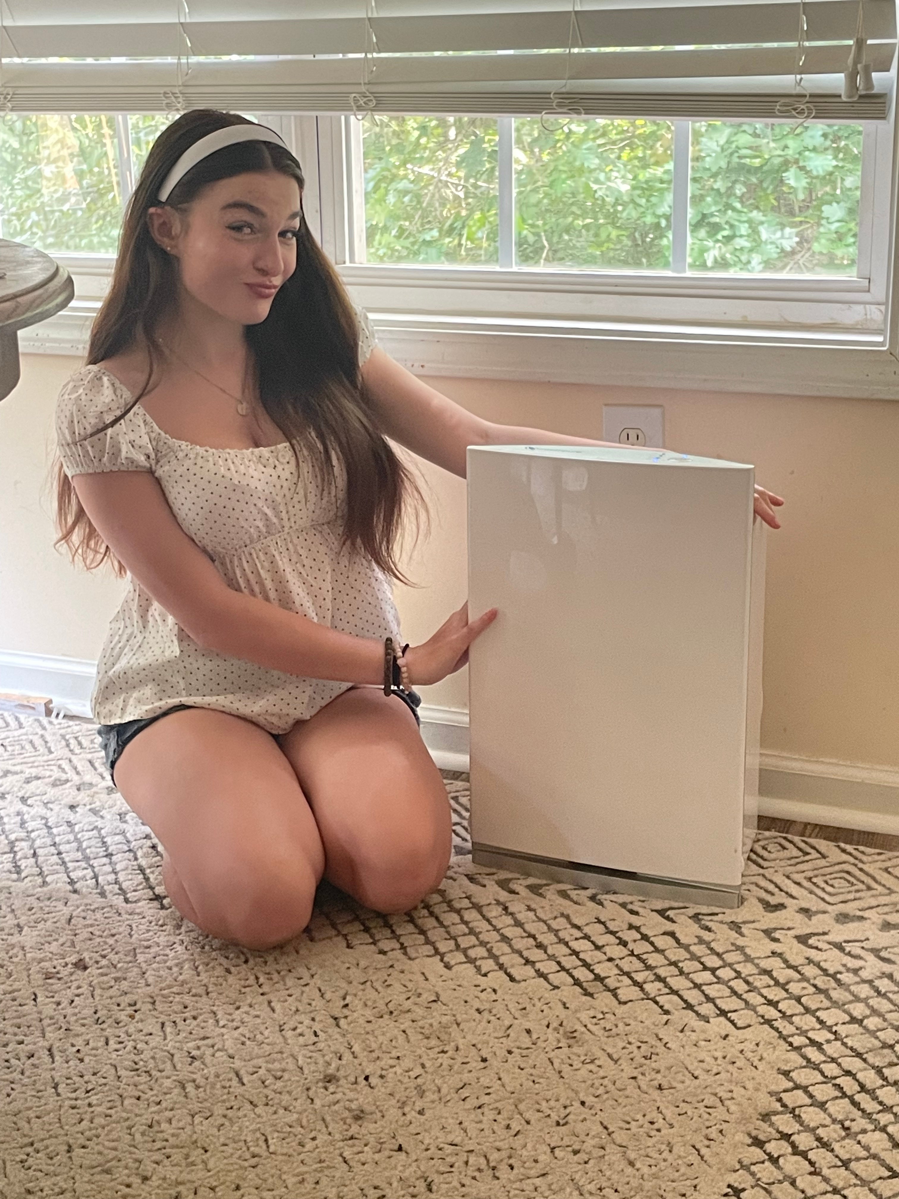 Woman sitting next to an air purifier on a carpeted floor.