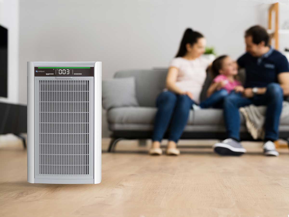 Air purifier on a wooden floor with a family sitting on a couch in the background
