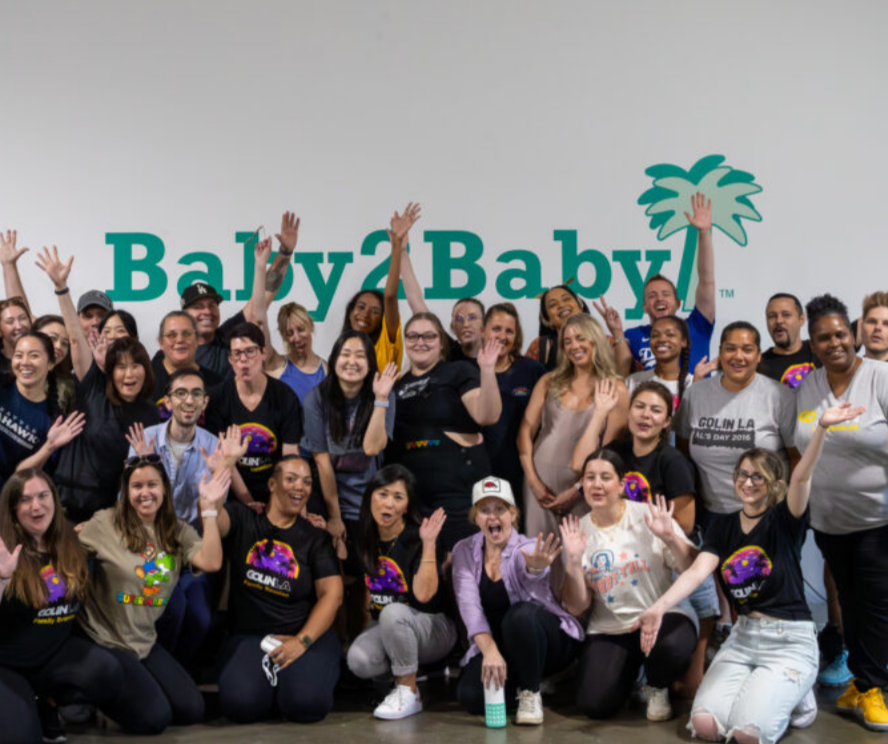 Group of people posing together in front of a Baby2Baby logo.