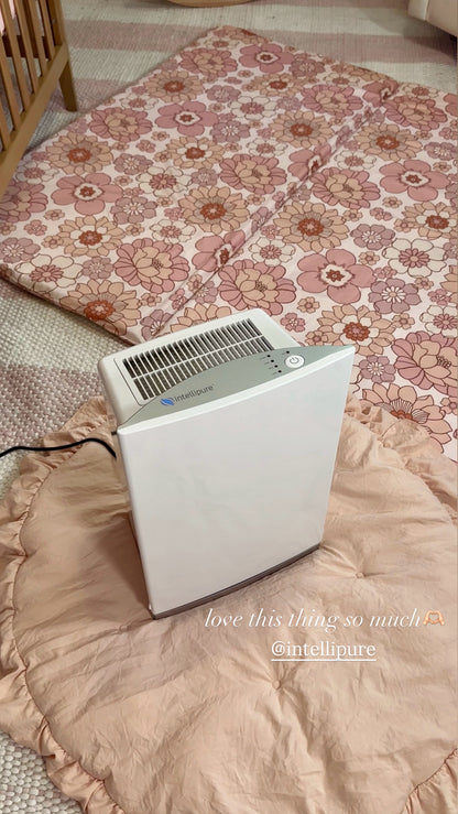Air purifier on a floral-patterned bedspread with visible brand name.