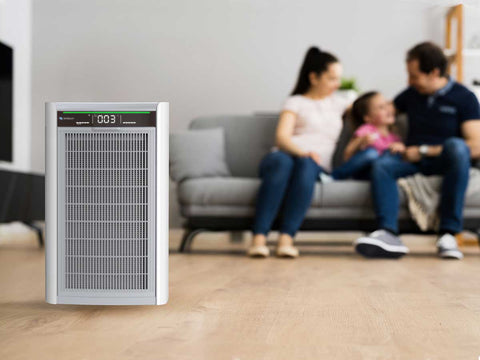 Air purifier on a wooden floor with a family sitting on a couch in the background