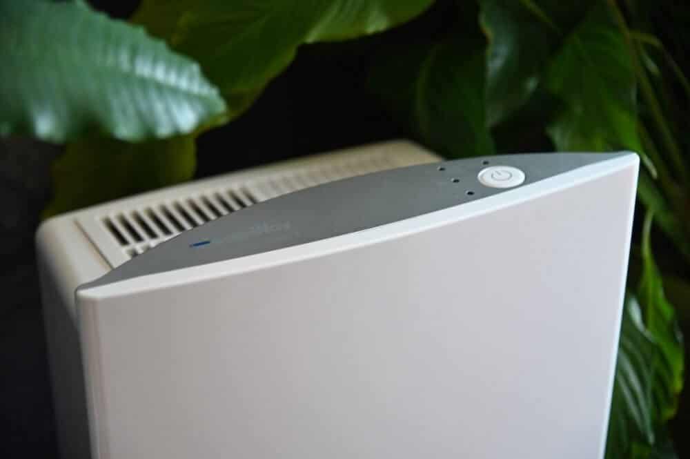 A zoomed in image of the Intellipure Compact air purifier with plants in the background. 